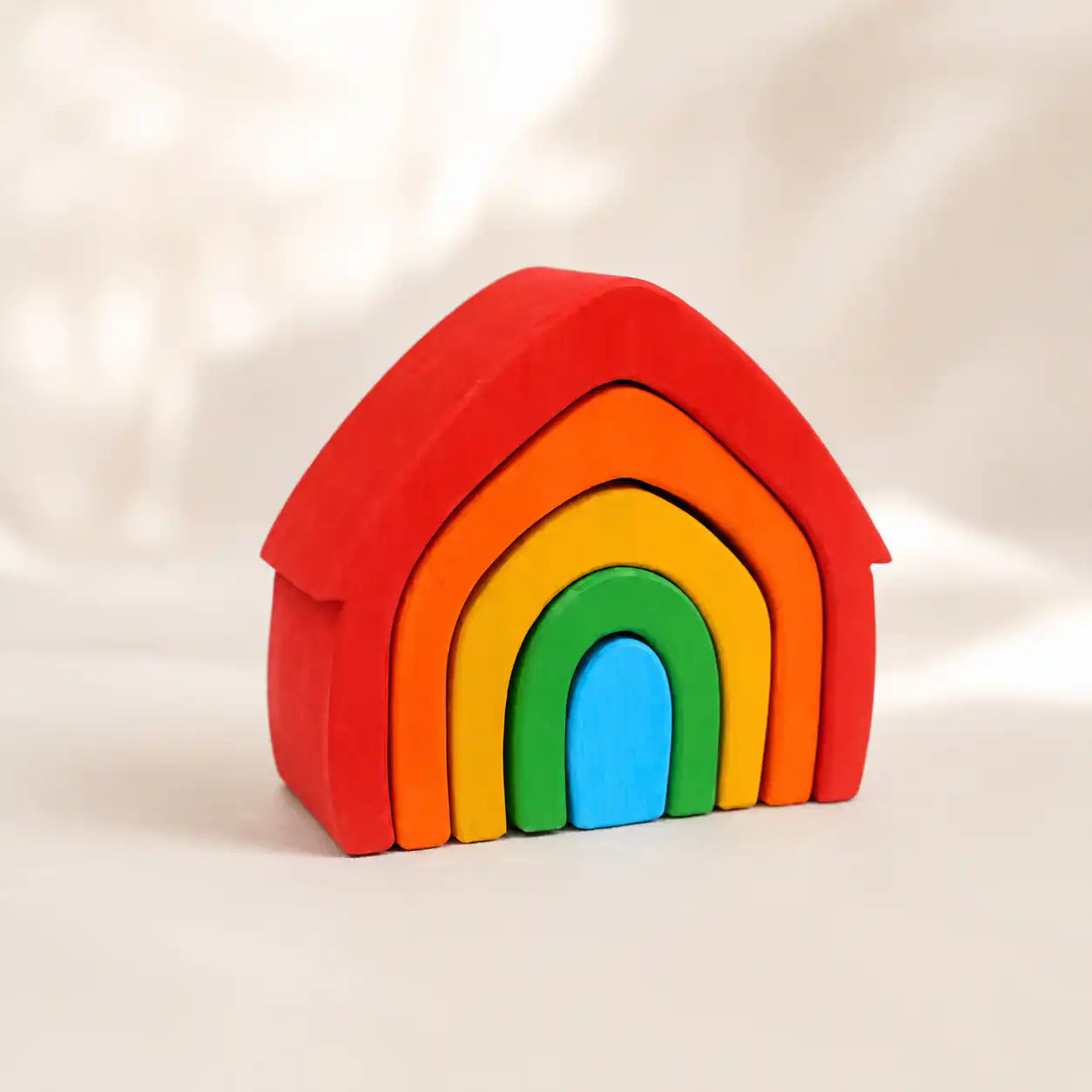 Wooden rainbow arch stacker with colorful nested arches on a soft cream surface, hero shot