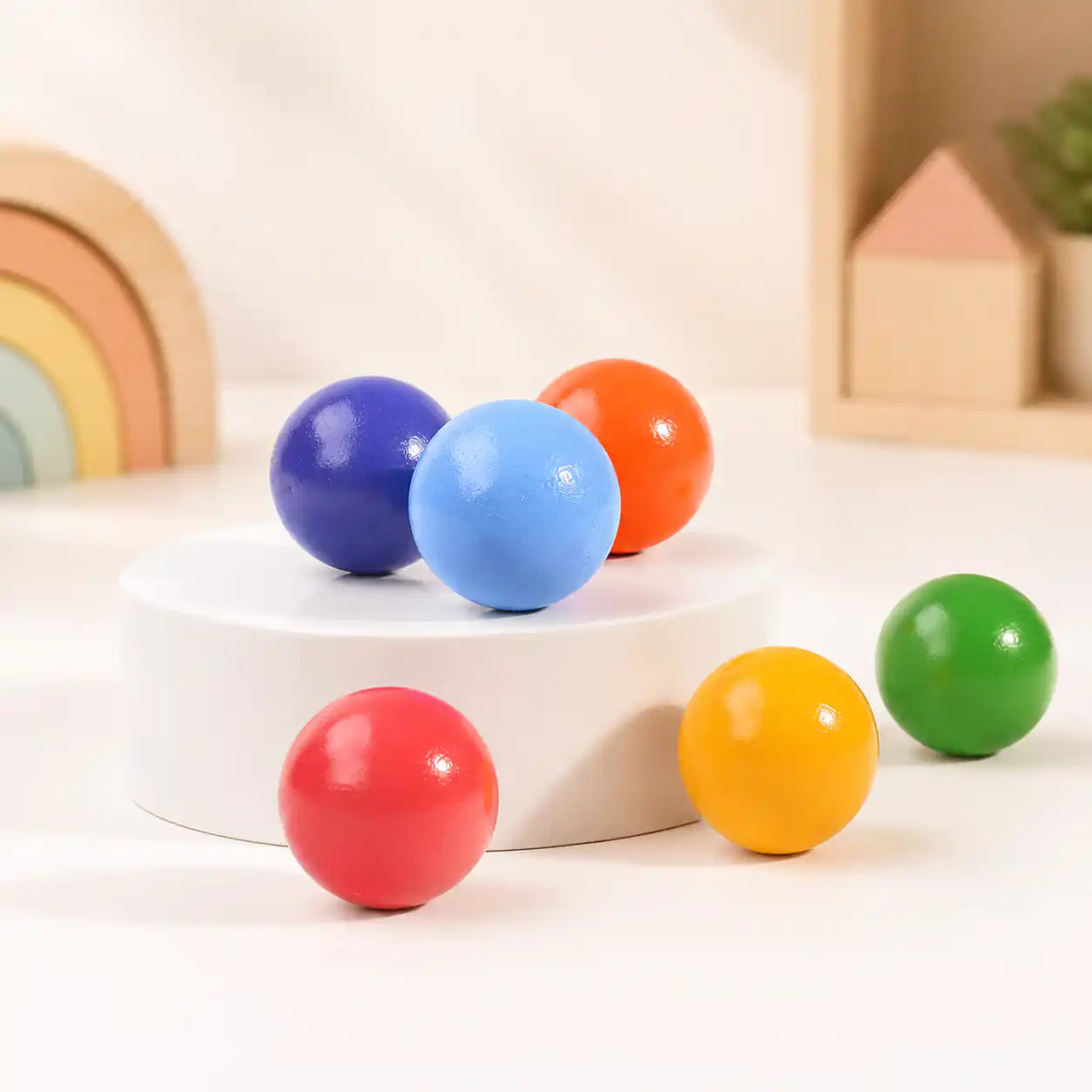 Wooden rainbow balls clustered together on a soft cream surface, hero shot