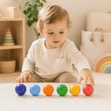 Wooden rainbow balls collected in a soft wooden bowl on a cream surface