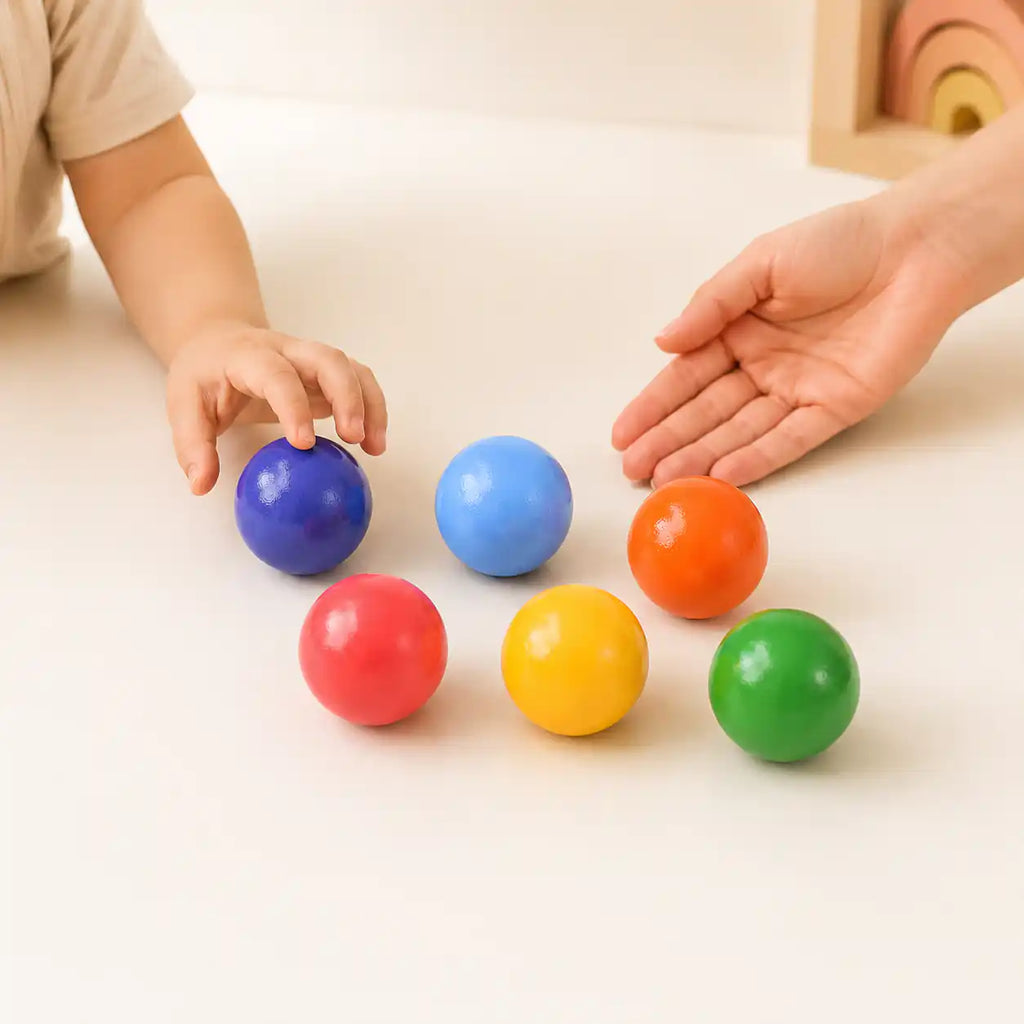 Top-down view of wooden rainbow balls scattered on a cream surface
