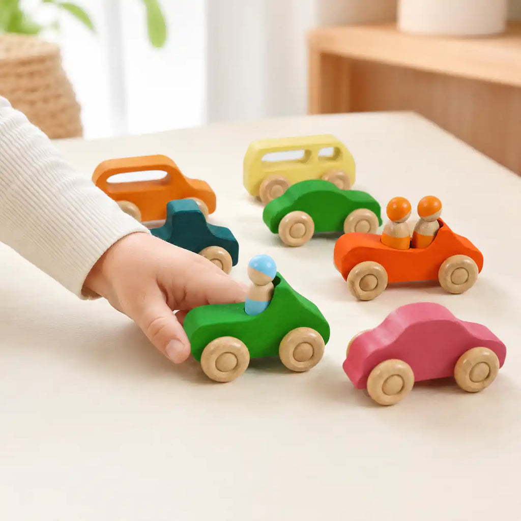 Wooden rainbow peg dolls arranged in front of the wooden car ready to climb in