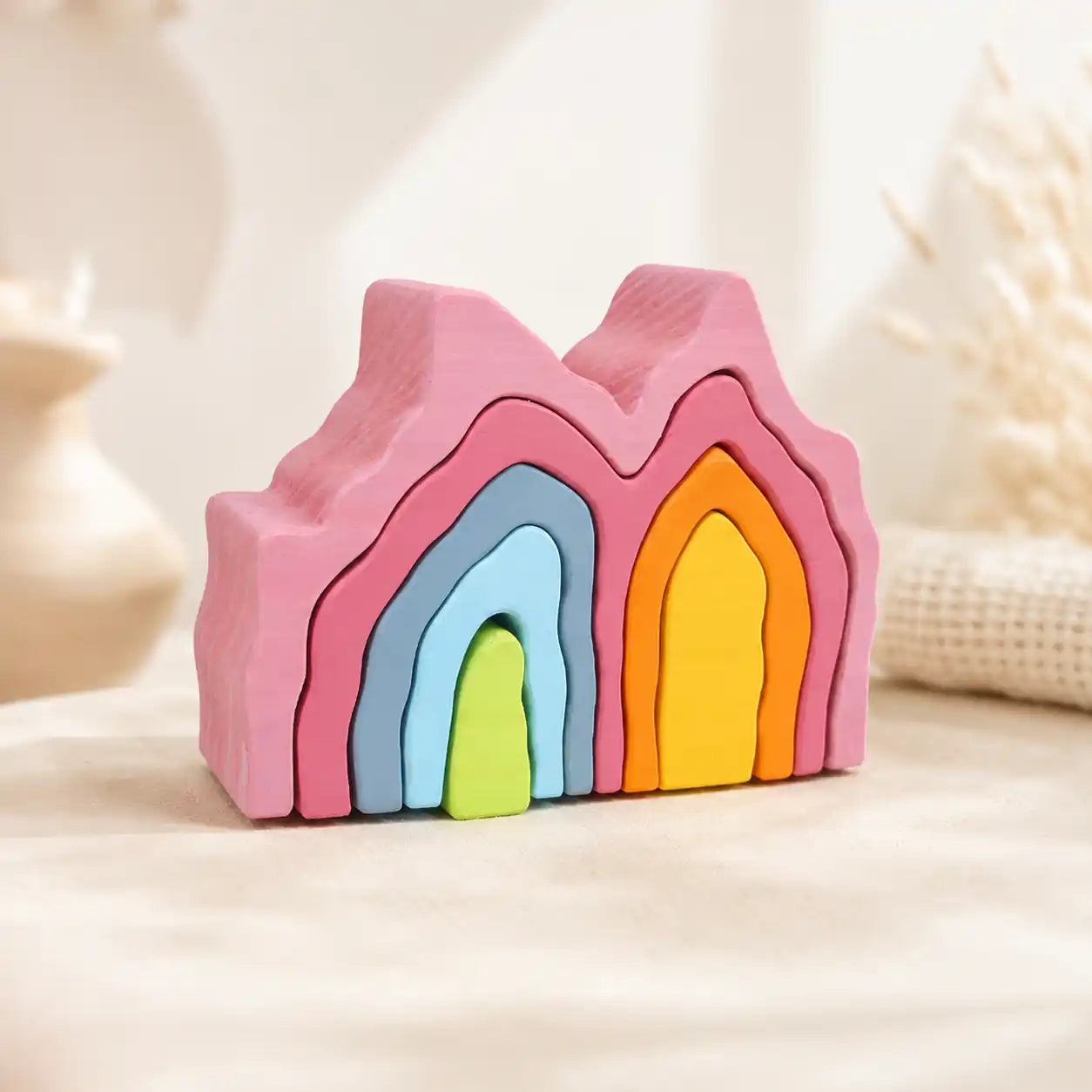 Wooden rainbow coral stacker with colorful coral-shaped pieces stacked on a soft cream surface, hero shot