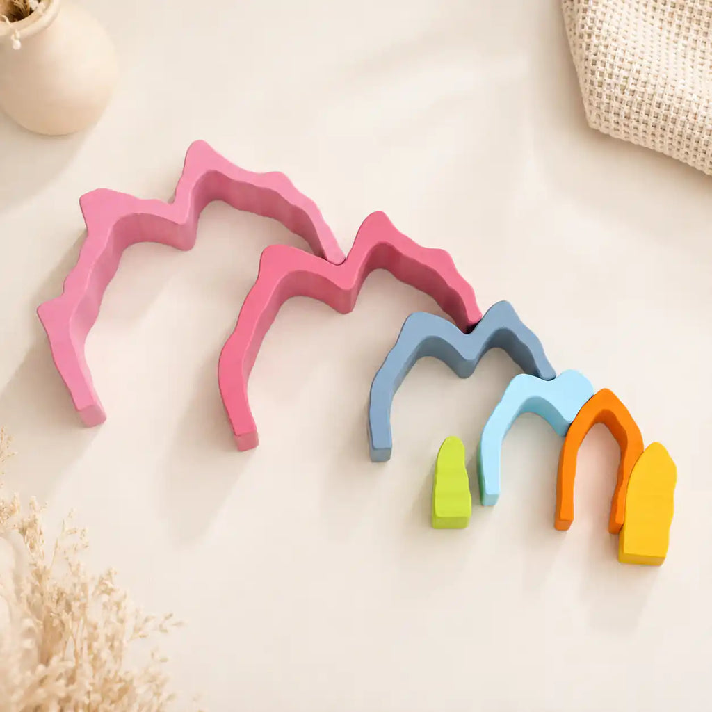 Wooden rainbow coral stacker pieces laid out separately on a cream surface showing each color