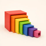 Small hands placing a wooden rainbow nesting cube into the next size up on a warm neutral surface