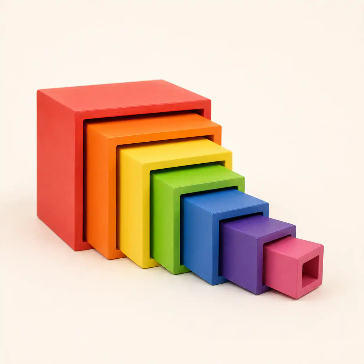 Small hands placing a wooden rainbow nesting cube into the next size up on a warm neutral surface
