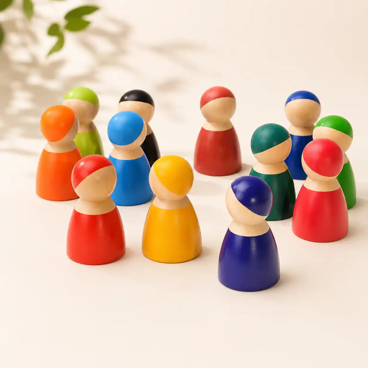 Wooden rainbow peg doll friends lined up in a row on a soft cream surface, hero shot