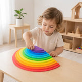 Preschool-age child placing the purple wooden semicircle on top of a fully nested rainbow stacker at a wooden table