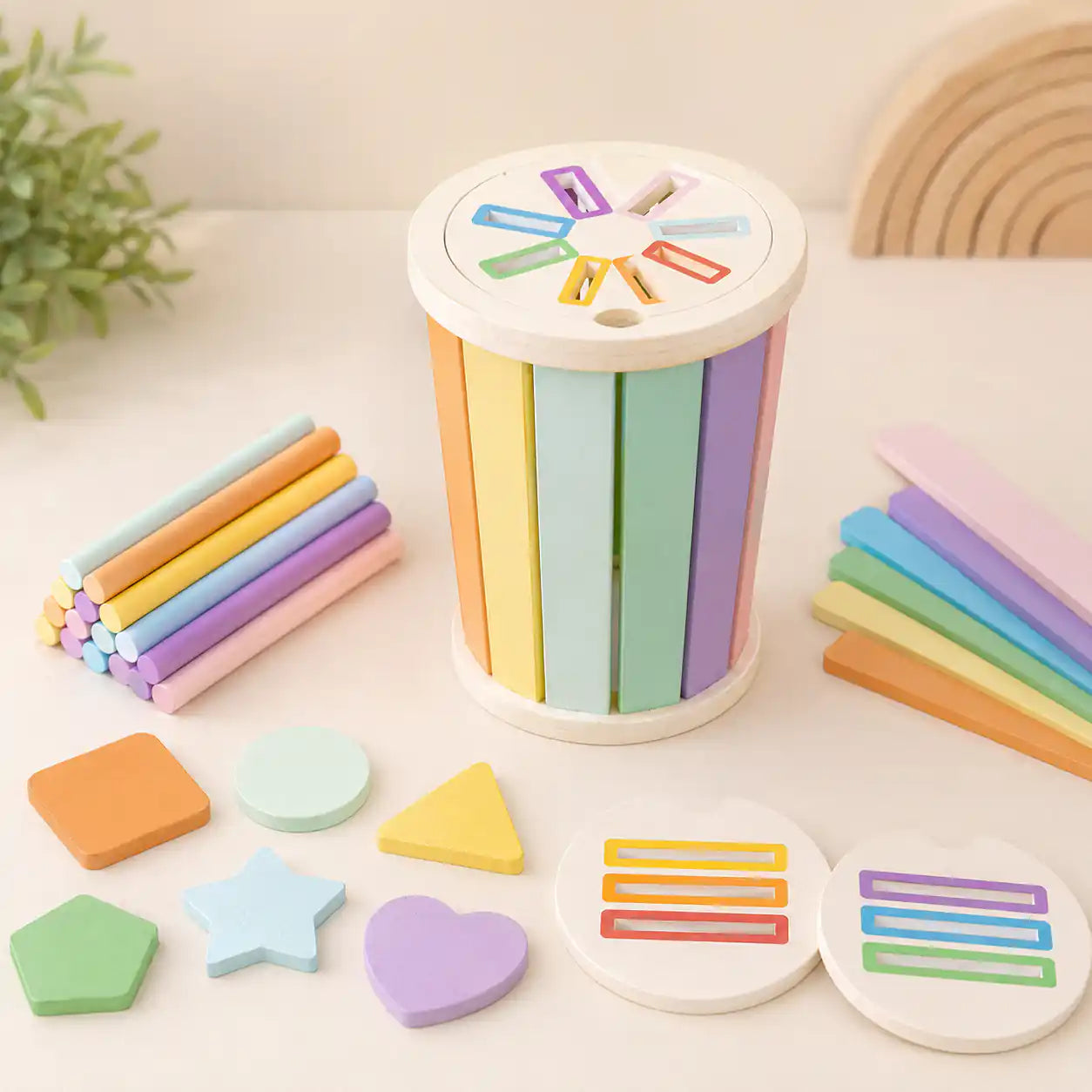Wooden rainbow sorting cylinder with pastel sticks, geometric shapes, sorting discs, and natural cotton storage bag on cream background