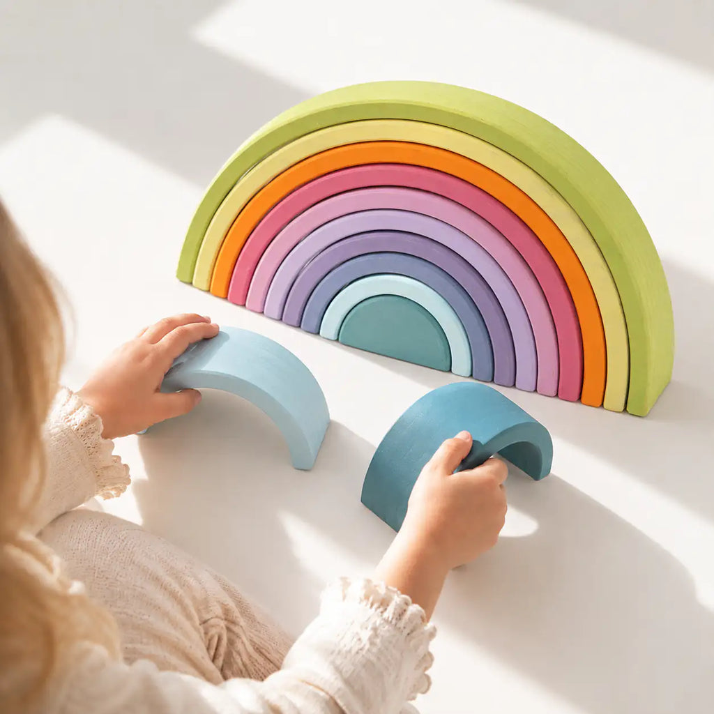 Toddler hands building with the 12-piece Macaron pastel wooden rainbow stacker during open-ended play