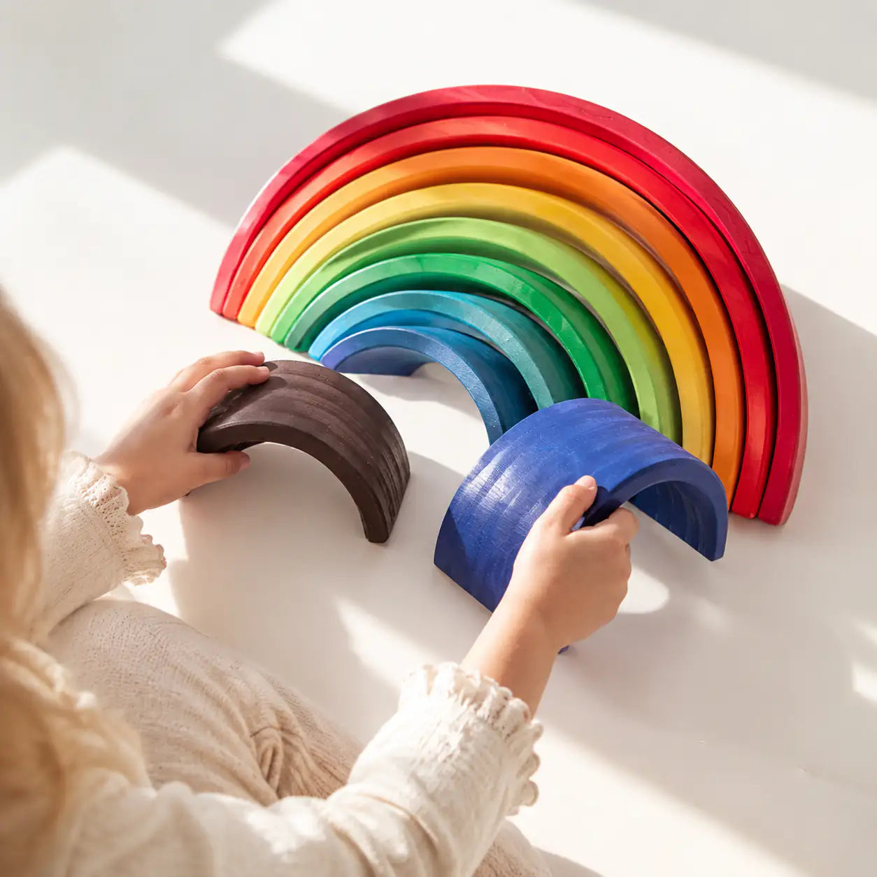 Toddler hands building with the 12-piece wooden rainbow stacker during open-ended play
