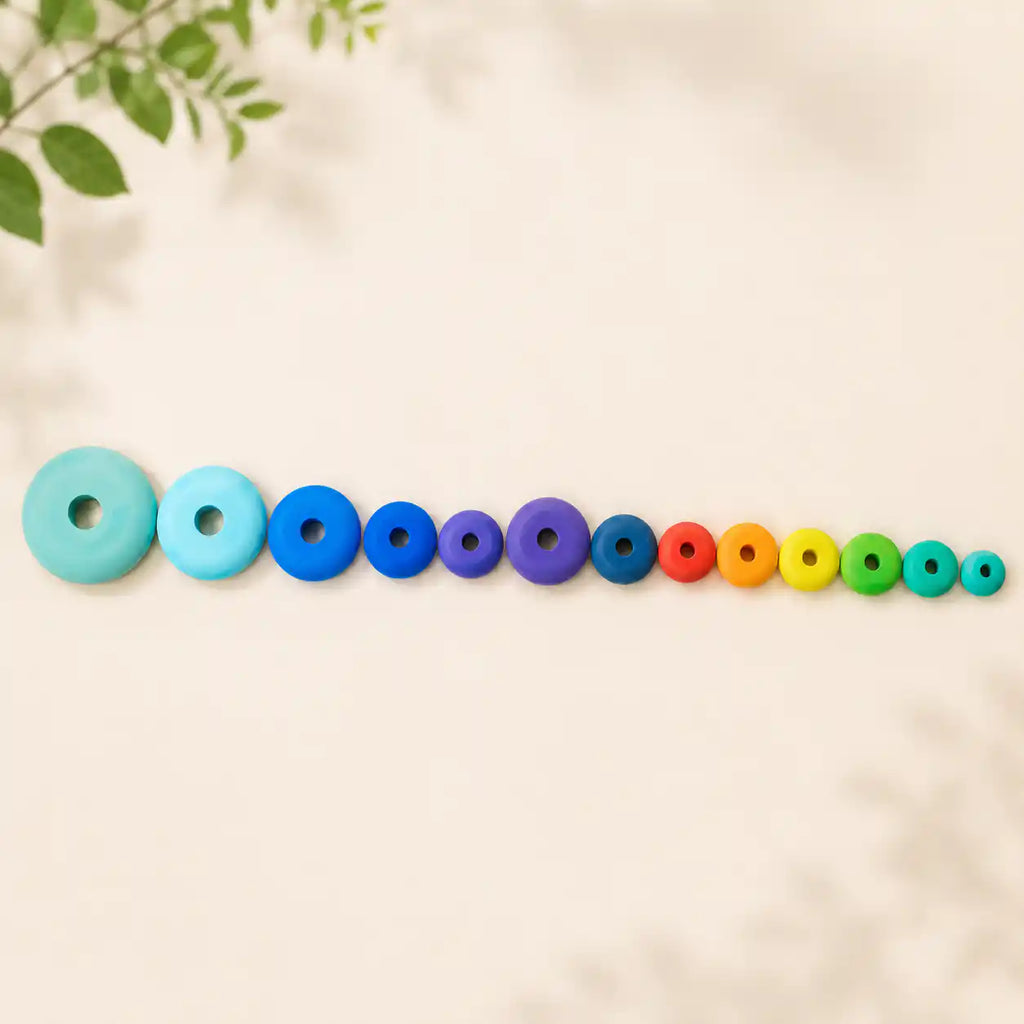 All twelve rainbow wooden stacking discs laid out in graduated size order on cream linen