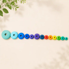 All twelve rainbow wooden stacking discs laid out in graduated size order on cream linen