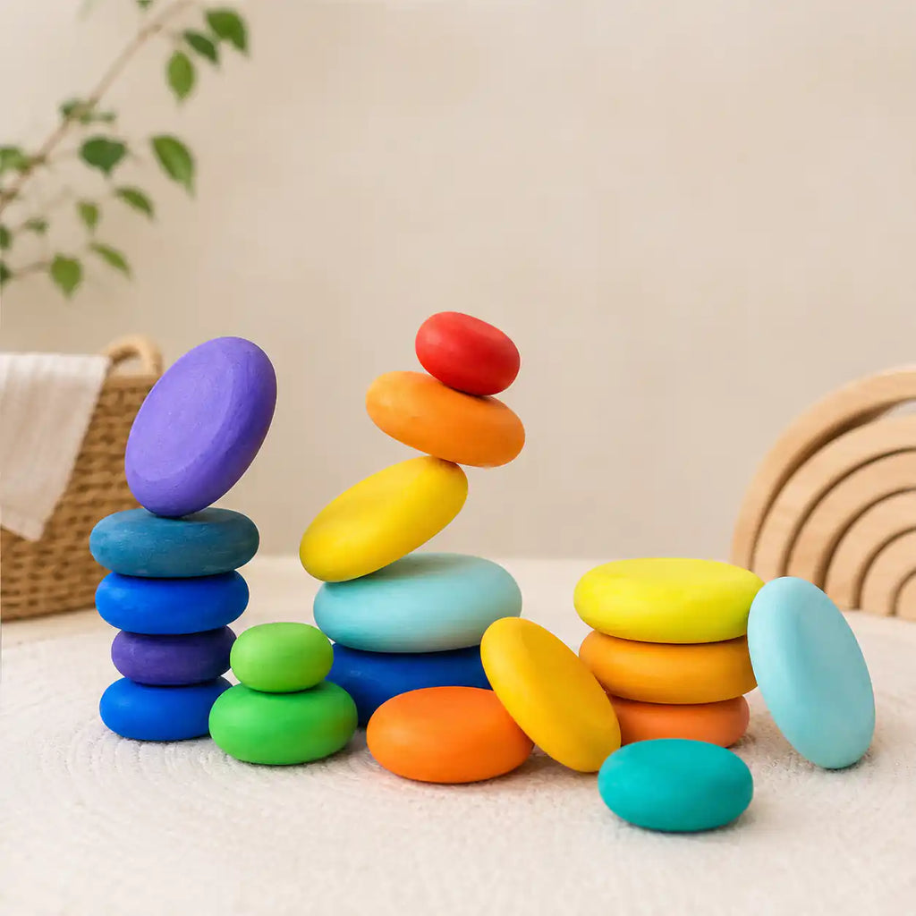 Wooden rainbow stacking discs arranged in several small balancing piles showing open-ended play options