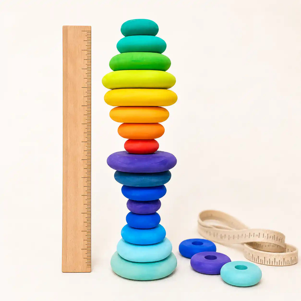 Wooden rainbow stacking discs tower beside a ruler and tape measure showing scale and size