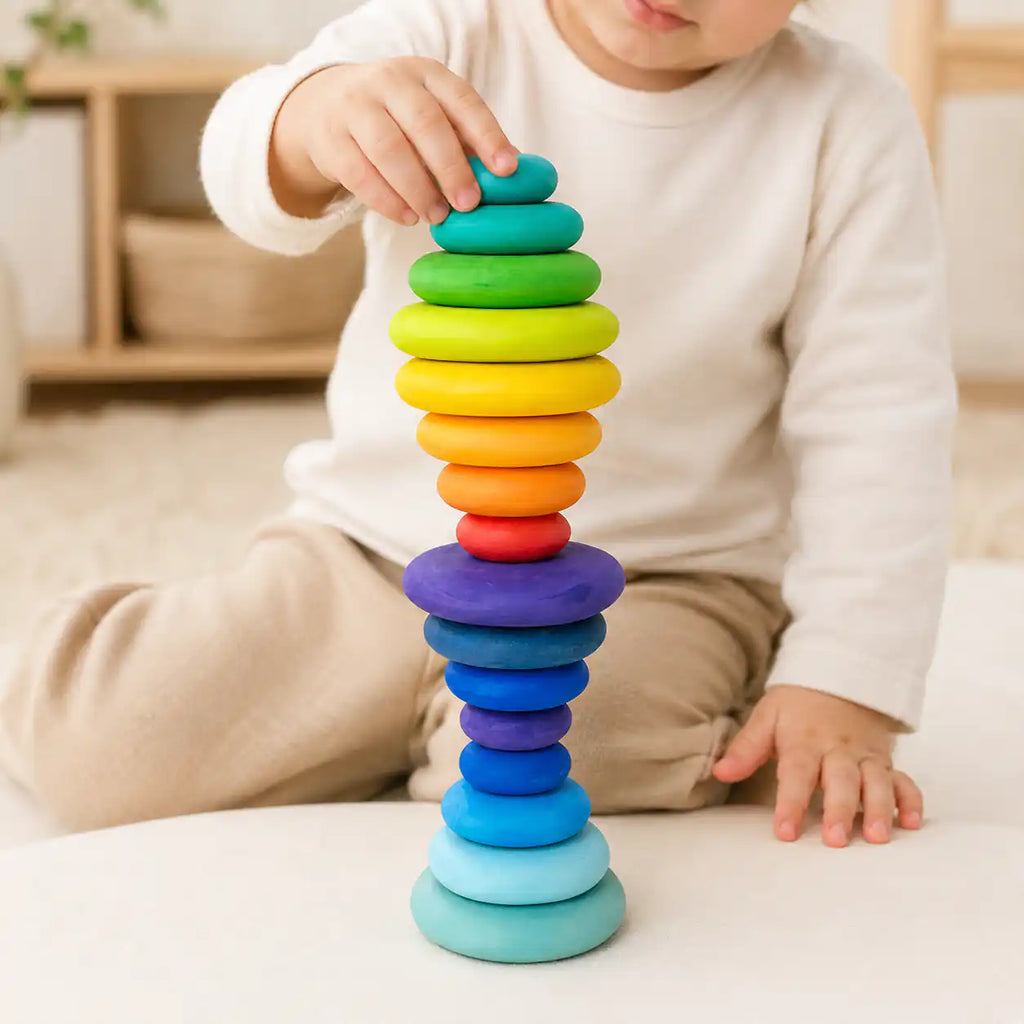 Toddler hands placing a small teal disc on top of a rainbow wooden stacking tower