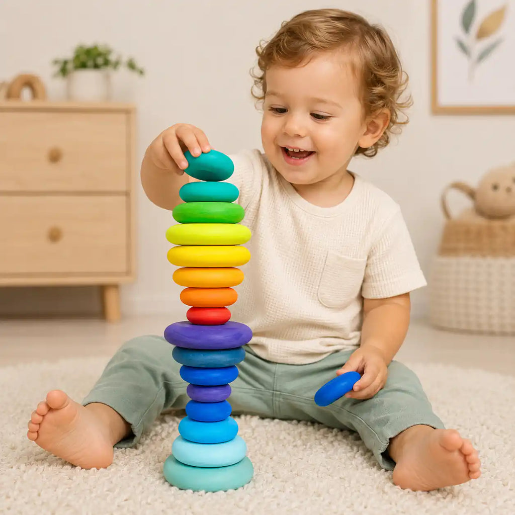 Young child smiling and stacking wooden rainbow discs into a tall tower on a soft nursery rug
