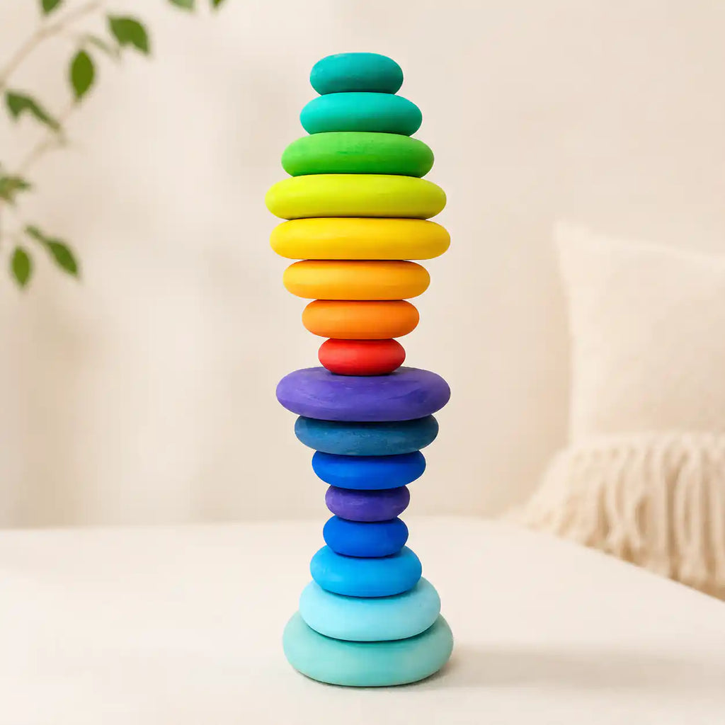 Wooden rainbow stacking discs balanced into a tall tower on a soft cream surface