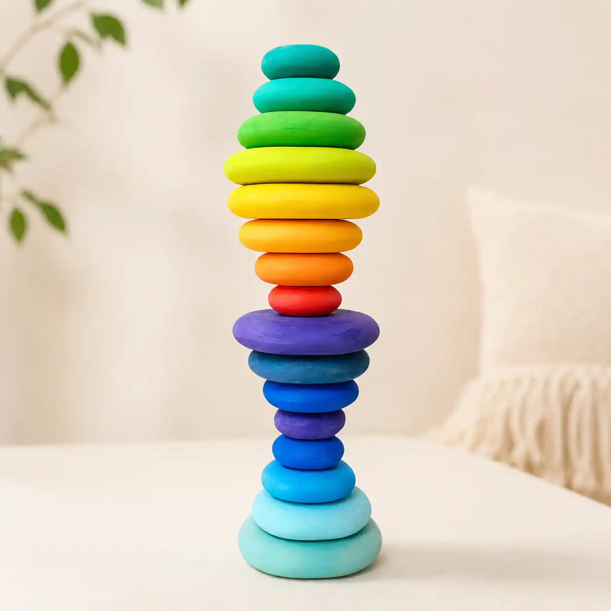 Wooden rainbow stacking discs balanced into a tall tower on a soft cream surface