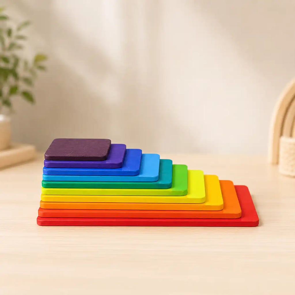 Small hands stacking a wooden rainbow tablet on top of the tower on a warm neutral surface