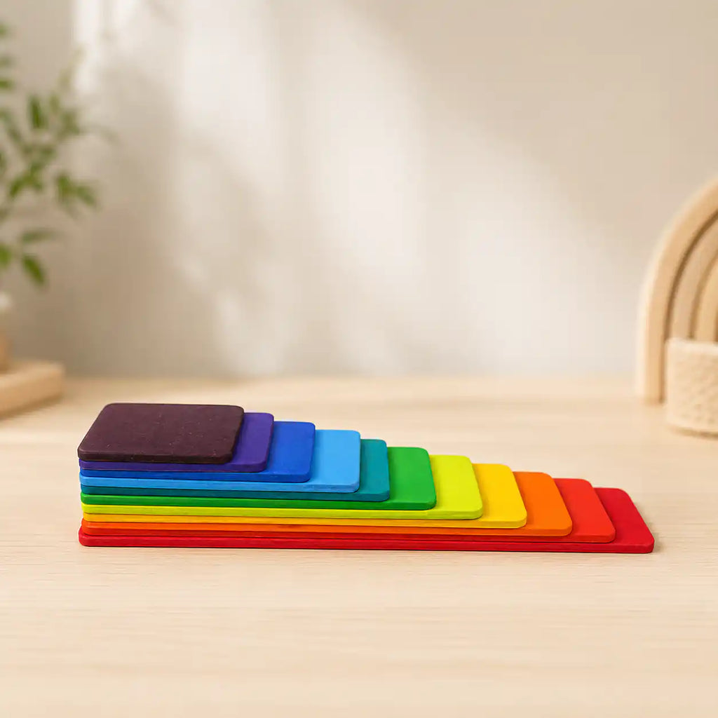 Wooden rainbow stacking tablets in a graduated tower on a soft cream surface, hero shot