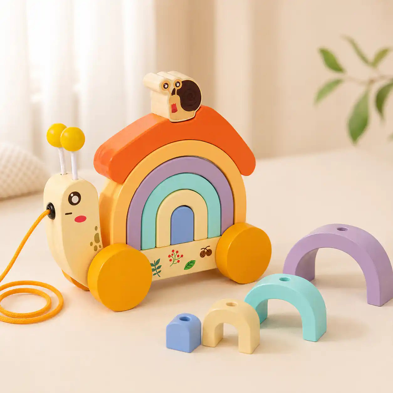 Wooden snail pull-along toy with detachable pastel rainbow stacker arches on cream background, Montessori toy for ages 1+