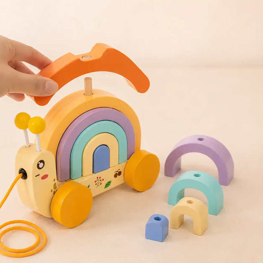 Wooden snail stacker with pastel arches restacked into a tall balance tower beside it for open-ended play