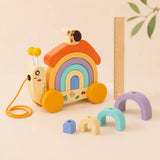 Wooden snail pull-along toy with pastel rainbow arches and small blue block laid out alongside on cream background