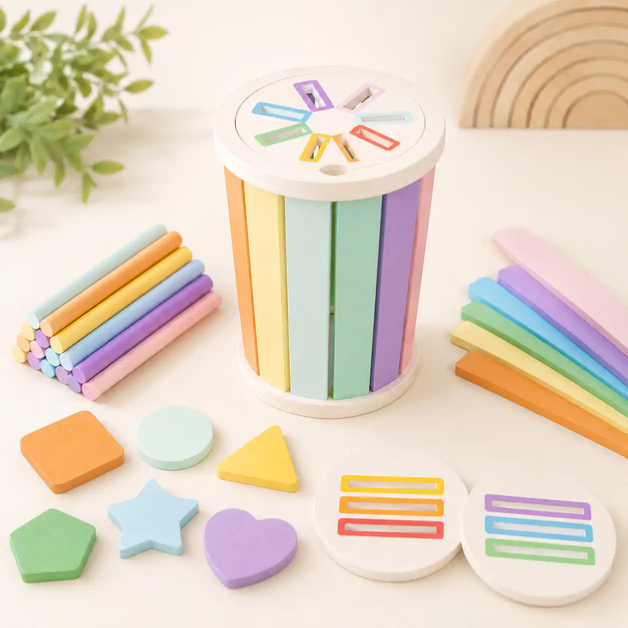 Wooden sorting cylinder with pastel shape pieces, dowels, and flat sticks arranged on cream tabletop